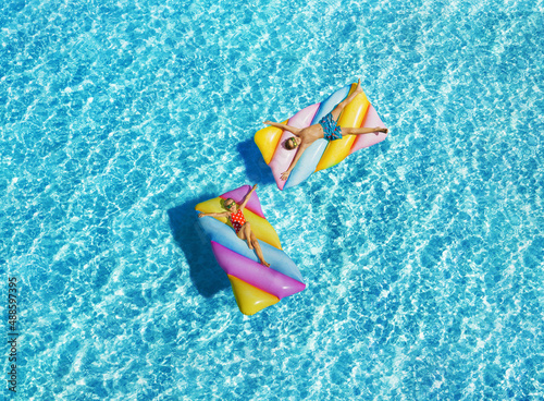 Child girl and boy on the inflatable mattress in the crystal clear water by the sea. Having fun on vacation at the hotel pool. Colorful vacation concept.