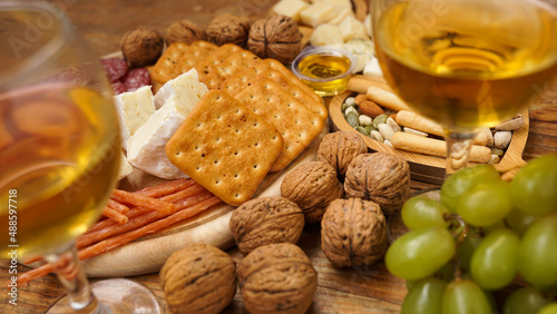 Snacks for wine. Cheese and meat plate. Sausages, cheese, nuts, grapes, crackers on wooden background. Two glasses of white wine.