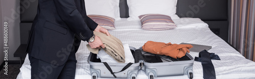 cropped view of man in suit unpacking suitcase in hotel room, banner