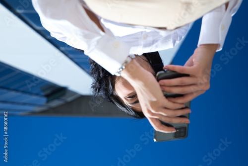 young, beautiful woman is consulting her mobile phone at the entrance door of the building where she works. The photo is taken from below and the building can be seen. Concept businesswoman.