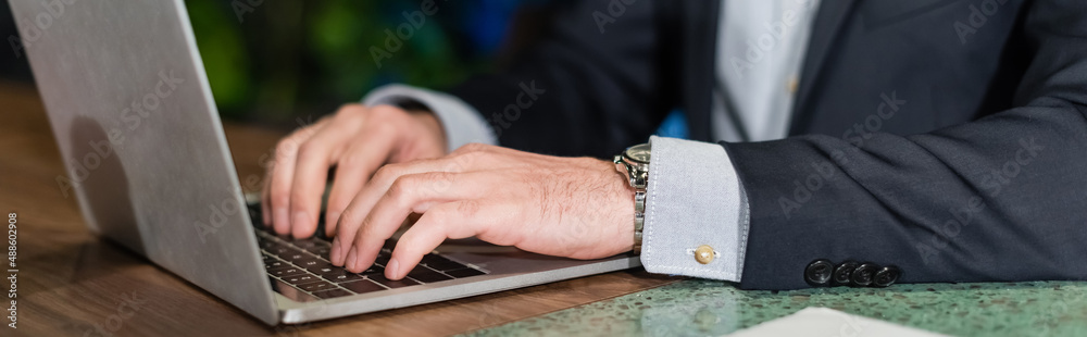 partial view of man in suit typing on laptop keyboard in hotel lobby, banner