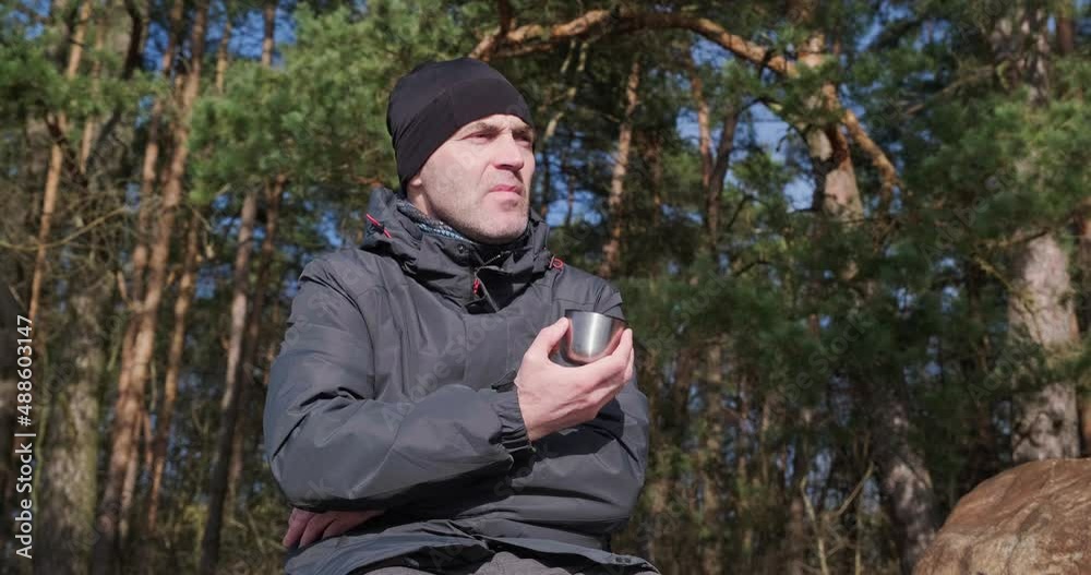 a man in warm clothes in a pine forest, holds a mug, says something and taps his fingers nervously a man in warm clothes in a pine forest, holds a mug, says something and taps his fingers nervously