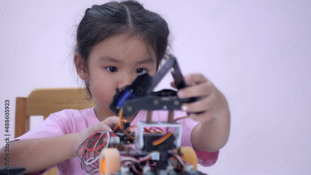 Slow motion scene of Asian girls in glasses holding a robot. A girls in a pink shirt and glasses sits at a table in front of him having a robot made by a girls. He is very satisfied with his work. Slow motion scene of Asian girls in glasses holding a robot. A girls in a pink shirt and glasses sits at a table in front of him having a robot made by a girls. He is very satisfied with his work.