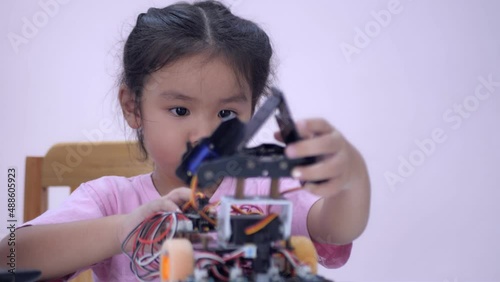 Slow motion scene of Asian girls in glasses holding a robot. A girls in a pink shirt and glasses sits at a table in front of him having a robot made by a girls. He is very satisfied with his work.