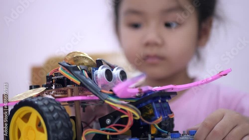 Slow motion scene of Asian girls in glasses holding a robot. A girls in a pink shirt and glasses sits at a table in front of him having a robot made by a girls. He is very satisfied with his work.