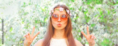 Portrait of beautiful young woman and flowers wearing floral headband, sunglasses on spring blooming garden background