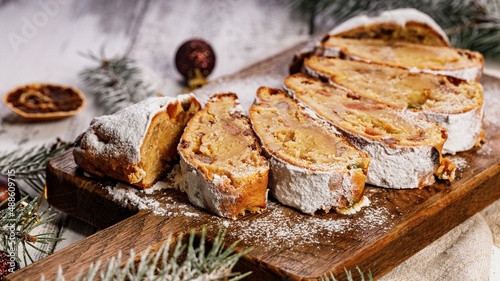 Food banner. Christmas stollen on a cutting board. Wooden white table background. Traditional Christmas pastry with marzipan, nuts, raisins and dried fruit.