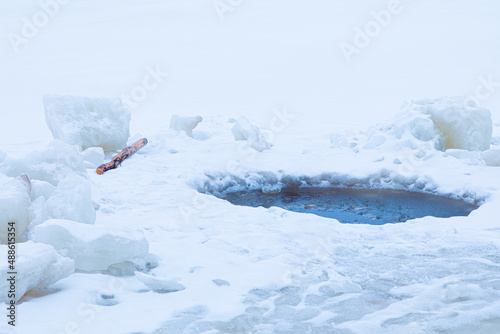 Beautiful winter landscape of bright, vivid and colorful ice hole among snow surface of lake, river or pound during snowfall or blizzard photo