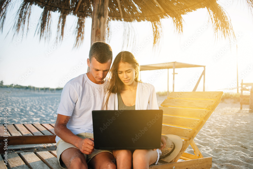 Happy smiling couple surf the net and enjoy summer on a tropical beach during sunset.