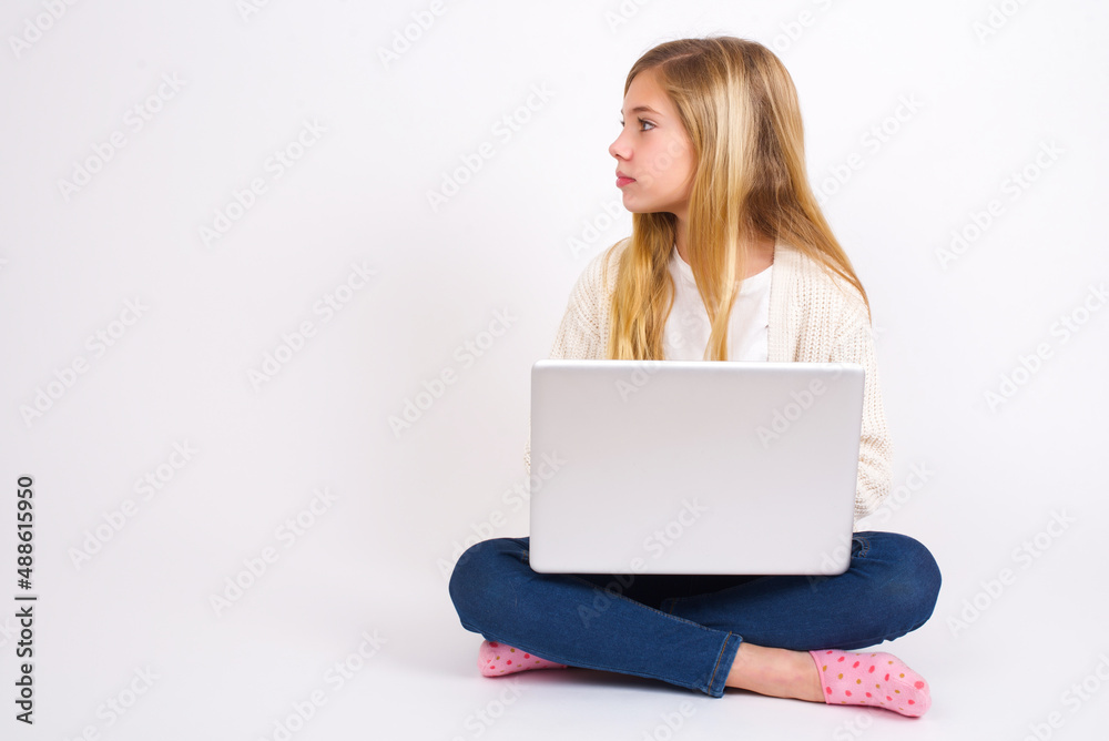 Side view of young happy smiling caucasian teen girl sitting with laptop in lotus position on white background Side view of young happy smiling caucasian teen girl sitting with laptop in lotus position on white background