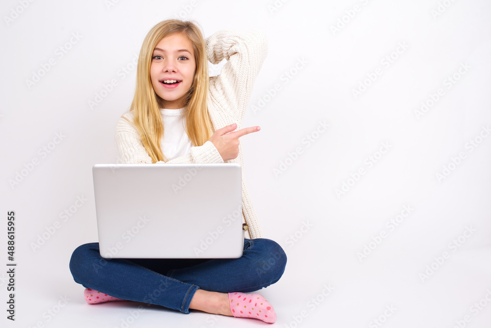 caucasian teen girl sitting with laptop in lotus position on white background feeling positive has amazed expression, indicates something. One hand on head and pointing with other hand. caucasian teen girl sitting with laptop in lotus position on white background feeling positive has amazed expression, indicates something. One hand on head and pointing with other hand.
