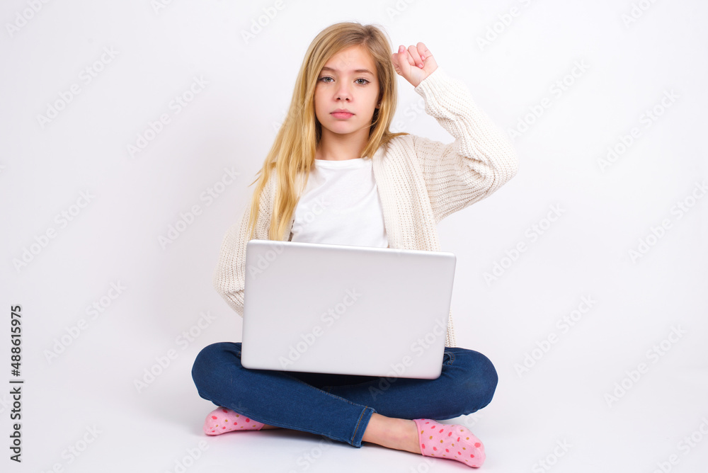 caucasian teen girl sitting with laptop in lotus position on white background feeling serious, strong and rebellious, raising fist up, protesting or fighting for revolution. caucasian teen girl sitting with laptop in lotus position on white background feeling serious, strong and rebellious, raising fist up, protesting or fighting for revolution.