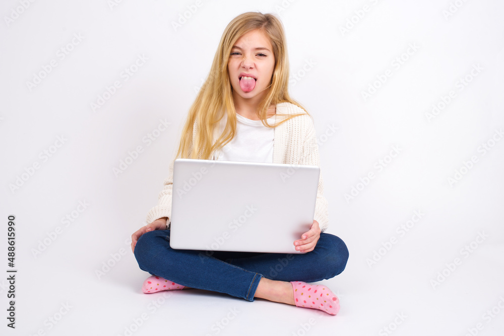 Body language. Disgusted stressed out caucasian teen girl sitting with laptop in lotus position on white background , frowning face, demonstrating aversion to something. Body language. Disgusted stressed out caucasian teen girl sitting with laptop in lotus position on white background , frowning face, demonstrating aversion to something.