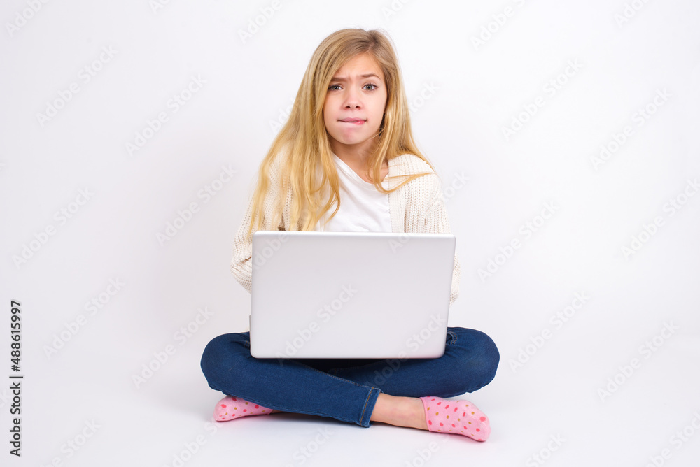 caucasian teen girl sitting with laptop in lotus position on white background being nervous and scared biting lips looking camera with impatient expression, pensive. caucasian teen girl sitting with laptop in lotus position on white background being nervous and scared biting lips looking camera with impatient expression, pensive.