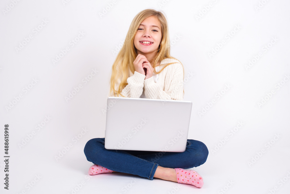 Dreamy charming caucasian teen girl sitting with laptop in lotus position on white background with pleasant expression, keeps hands crossed near face, excited about something pleasant. Dreamy charming caucasian teen girl sitting with laptop in lotus position on white background with pleasant expression, keeps hands crossed near face, excited about something pleasant.