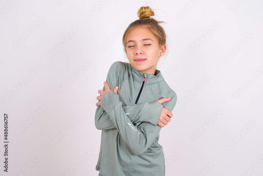 little caucasian kid girl with hair bun wearing technical shirt over white background Hugging oneself happy and positive, smiling confident. Self love and self care little caucasian kid girl with hair bun wearing technical shirt over white background Hugging oneself happy and positive, smiling confident. Self love and self care