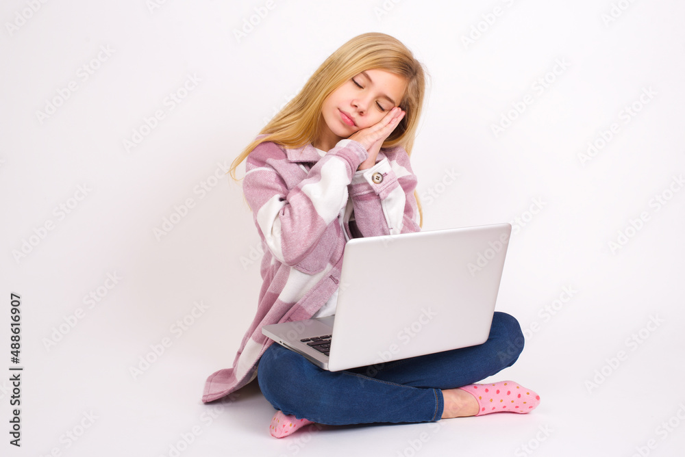 Relax and sleep time. Tired caucasian teen girl sitting with laptop in lotus position on white background with closed eyes leaning on palms making sleeping gesture. Relax and sleep time. Tired caucasian teen girl sitting with laptop in lotus position on white background with closed eyes leaning on palms making sleeping gesture.