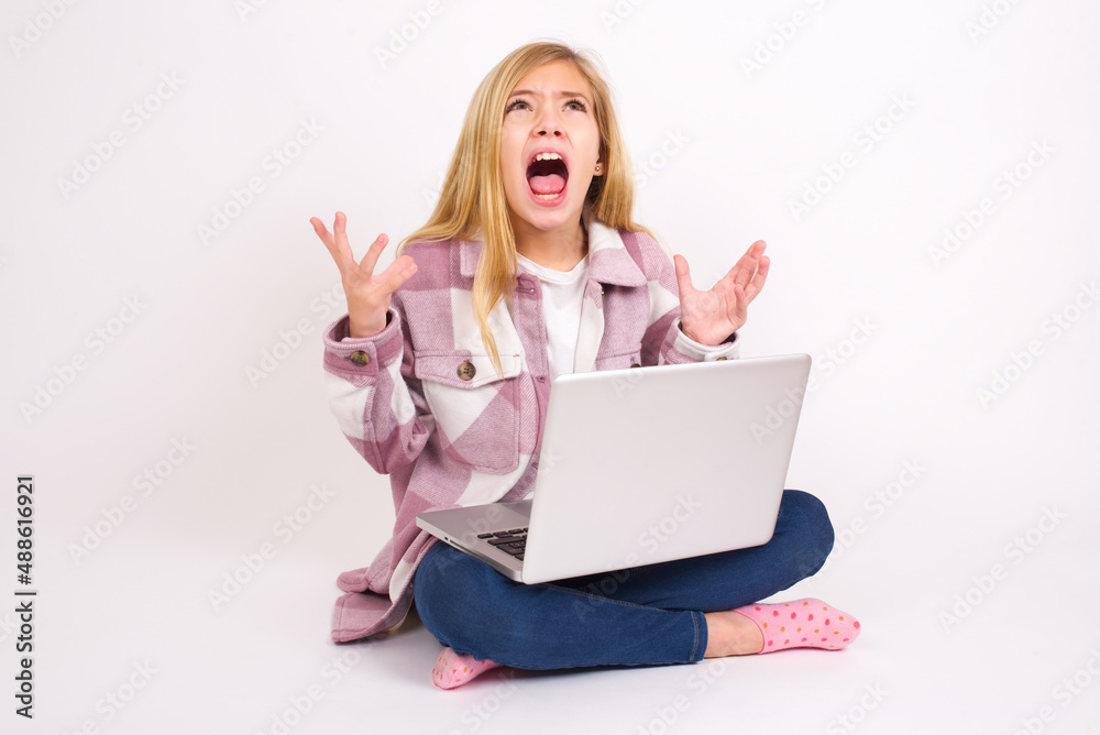 caucasian teen girl sitting with laptop in lotus position on white background crying and screaming. Human emotions, facial expression concept. Screaming, hate, rage. caucasian teen girl sitting with laptop in lotus position on white background crying and screaming. Human emotions, facial expression concept. Screaming, hate, rage.