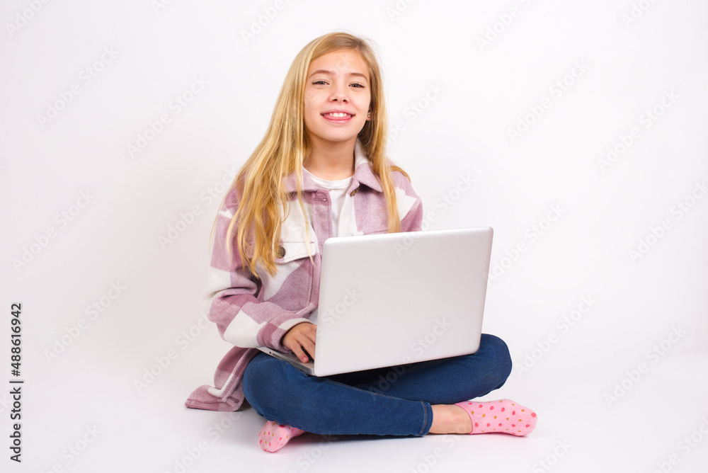 caucasian teen girl sitting with laptop in lotus position on white background with happy and funny face smiling and showing tongue. caucasian teen girl sitting with laptop in lotus position on white background with happy and funny face smiling and showing tongue.