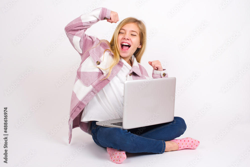 Yes I am winner. Charming delighted and excited caucasian teen girl sitting with laptop in lotus position raising up fist in triumph and victory smiling achieving success grinning from delight. Yes I am winner. Charming delighted and excited caucasian teen girl sitting with laptop in lotus position raising up fist in triumph and victory smiling achieving success grinning from delight.