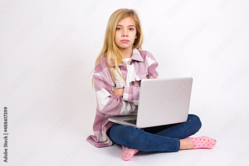 Picture of angry caucasian teen girl sitting with laptop in lotus position on white background looking camera. Picture of angry caucasian teen girl sitting with laptop in lotus position on white background looking camera.