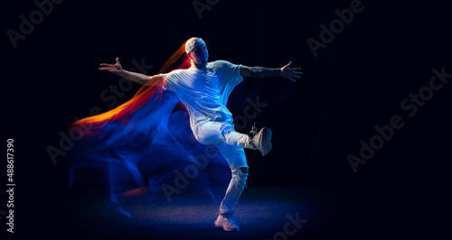 Split personality. Sportive man in sports white uniform and do-rag dancing hip-hop isolated on dark background in mixed neon light. Youth culture, style and fashion