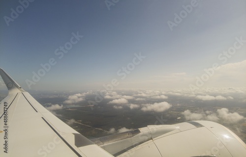 Beautiful view of aircraft wing look from cabin window. Blue sky, white clouds and land in below.