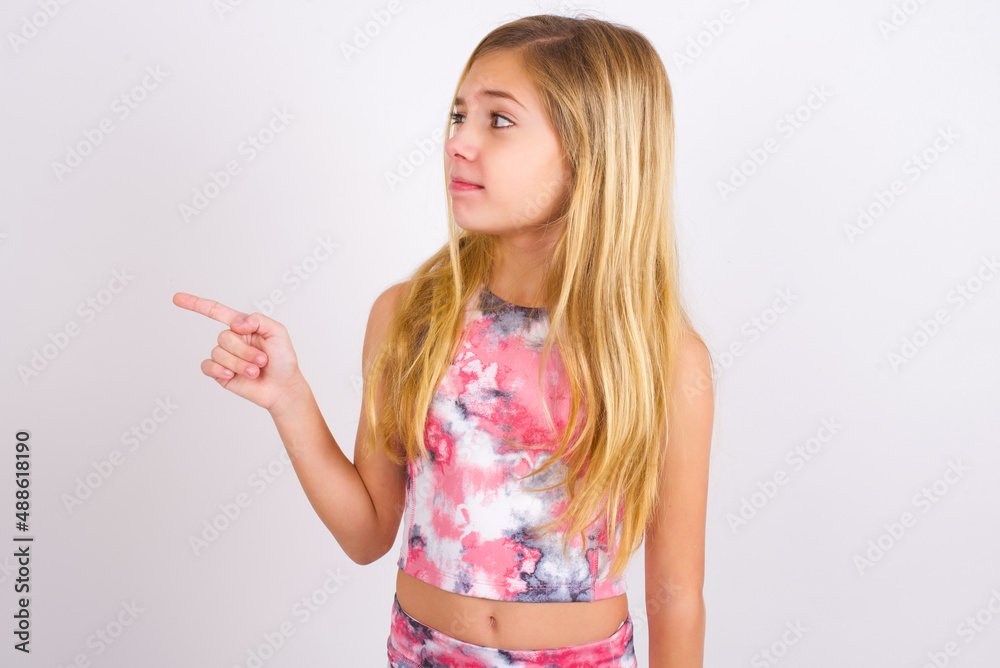 little caucasian kid girl wearing sport clothing over white background points at copy space and advertises something, advices best price. little caucasian kid girl wearing sport clothing over white background points at copy space and advertises something, advices best price.