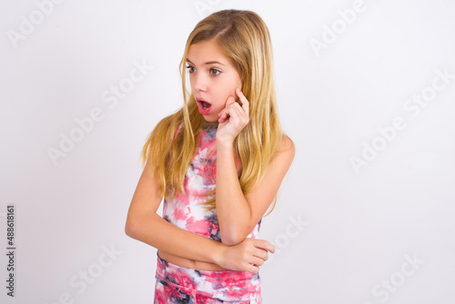 Astonished little caucasian kid girl wearing sport clothing over white background looks aside surprisingly with opened mouth. photo