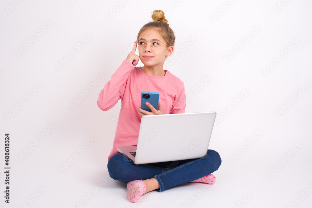 Beautiful caucasian teen girl sitting with laptop in lotus position on white background holding gadget while sticking out tongue Beautiful caucasian teen girl sitting with laptop in lotus position on white background holding gadget while sticking out tongue