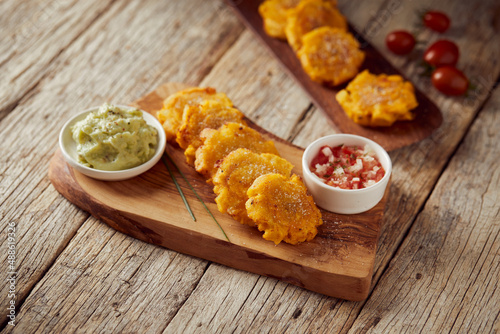 Patacones or tostones, typical Ecuadorian appetizer that consists on fried green plantain slices. It’s accompanied with guacamole and served on a traditional plate with a wooden and rustic background. photo