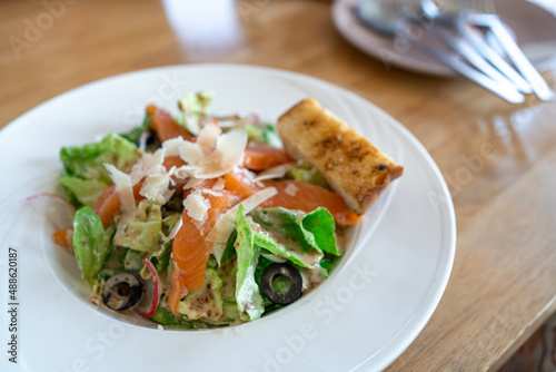 fresh Salmon salad with fresh green leaves and black olive on white plate.