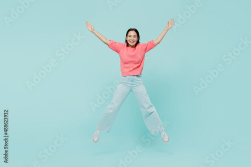 Full body young smiling fun happy woman of Asian ethnicity 20s wearing pink sweater jumpo high with outstretched hands isolated on pastel plain light blue color background. People lifestyle concept.