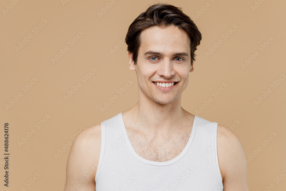 Attractive handsome smiling fun cheerful young man 20s perfect skin wearing undershirt look camera isolated on pastel pastel beige background studio Skin care healthcare cosmetic procedures concept. Attractive handsome smiling fun cheerful young man 20s perfect skin wearing undershirt look camera isolated on pastel pastel beige background studio Skin care healthcare cosmetic procedures concept.