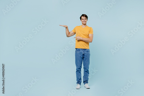 Full body smiling happy fun young man 20s wearing yellow t-shirt show hight measurement scale with hands arms isolated on plain pastel light blue background studio portrait. People lifestyle concept. photo