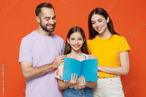 Young parents mom dad with child daughter teen girl wear basic t-shirts read book with kid help to do hometask isolated on yellow background studio portrait. Family day parenthood childhood concept photo