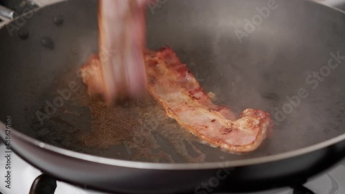 The process of preparing breakfast with bacon. Flipping bacon pieces.