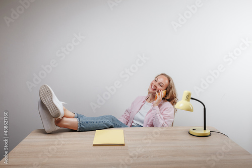 a cute girl sits with her feet on the table and talks on the phone