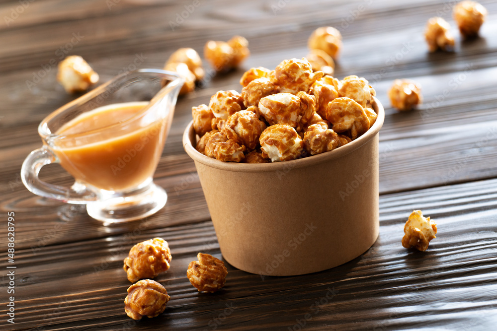 Caramelized popcorn in paper bucket on wooden table