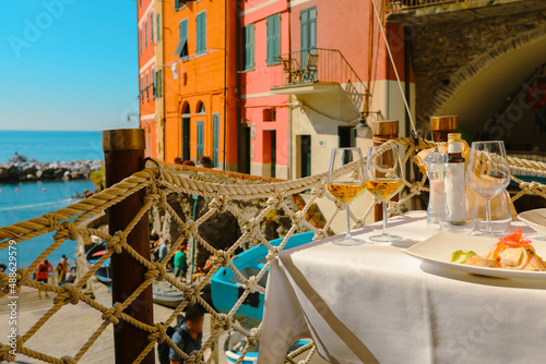 Fototapeta Naklejka Na Ścianę i Meble -  Two glasses of white wine on table with a plate of and view on old street in  village