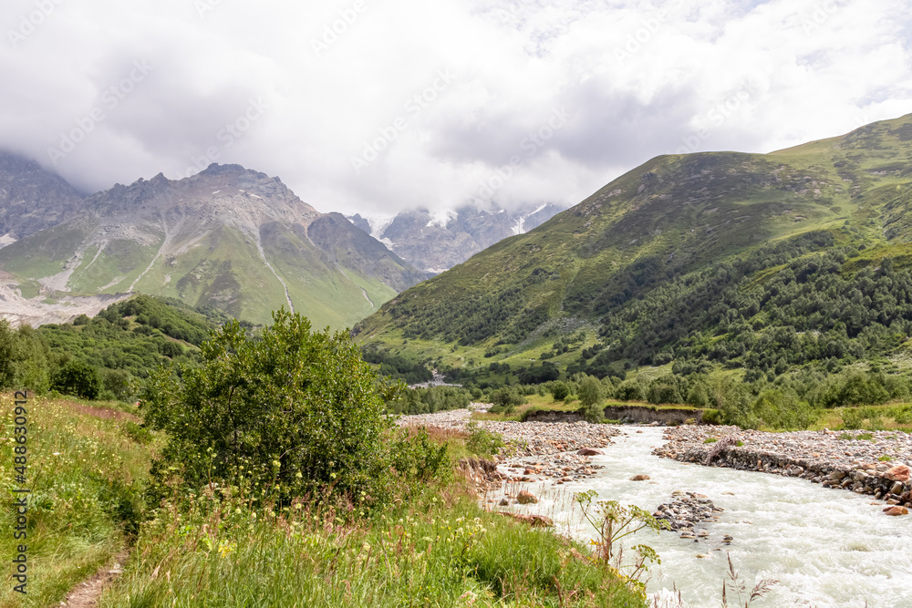 Patara Enguri River flowing down the a valley in the Greater Caucasus Mountain Range in Georgia, Svaneti Region, Ushguli. The Shkhara Mountain is covered by clouds. Snow-capped mountains.Glacier