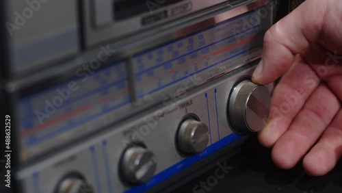 A hand turns the frequency knob on an old gray tape recorder - close-up