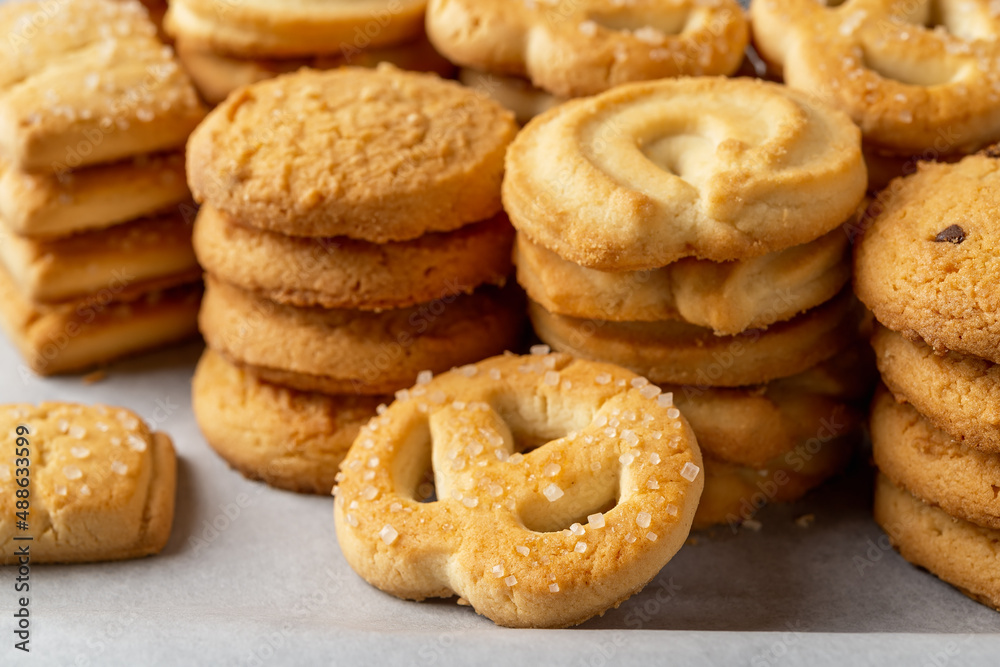 Sugar pretzel against of stacked shortbread cookies on a white baking parchment. Assorted crispy butter biscuits close-up. Tasty baked pastry. Breakfast, snack and sweet food concepts.