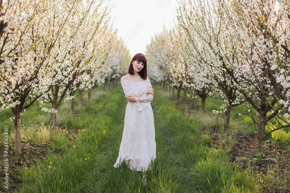 Sensual young lady in light white dress smiling and looking at camera while posing outdoors. Leisure time spending at beautiful blooming spring garden. Sensual young lady in light white dress smiling and looking at camera while posing outdoors. Leisure time spending at beautiful blooming spring garden.