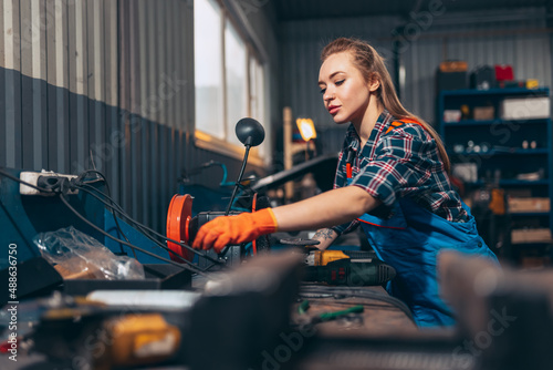 Female auto mechanic. beautiful young red-headed girl in working process at auto service station, indoors. Gender equality. Work, occupation, fashion, job
