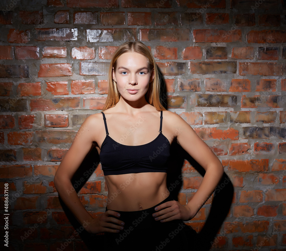 Young fit pretty woman dressed in sport clothes poses against brick wall. Young fit pretty woman dressed in sport clothes poses against brick wall.