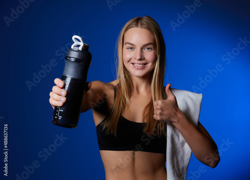 Sports girl, with a towel on her shoulder, points her finger at a bottle of water. © Ryzhkov Oleksandr