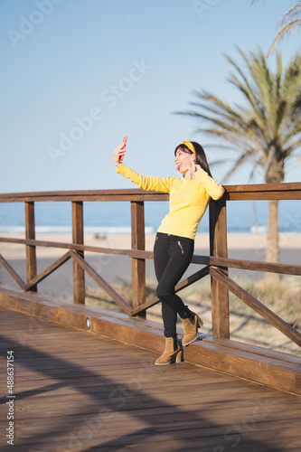 Vertical poto of a woman gesturing victory to the camera of a mobile on a bridge next to the sea