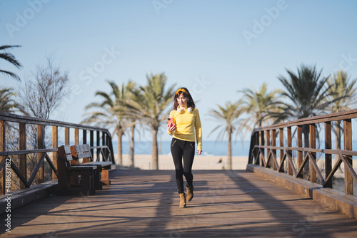 Beauty woman using the mobil while walking across a bridge next to the beach in a sunny day