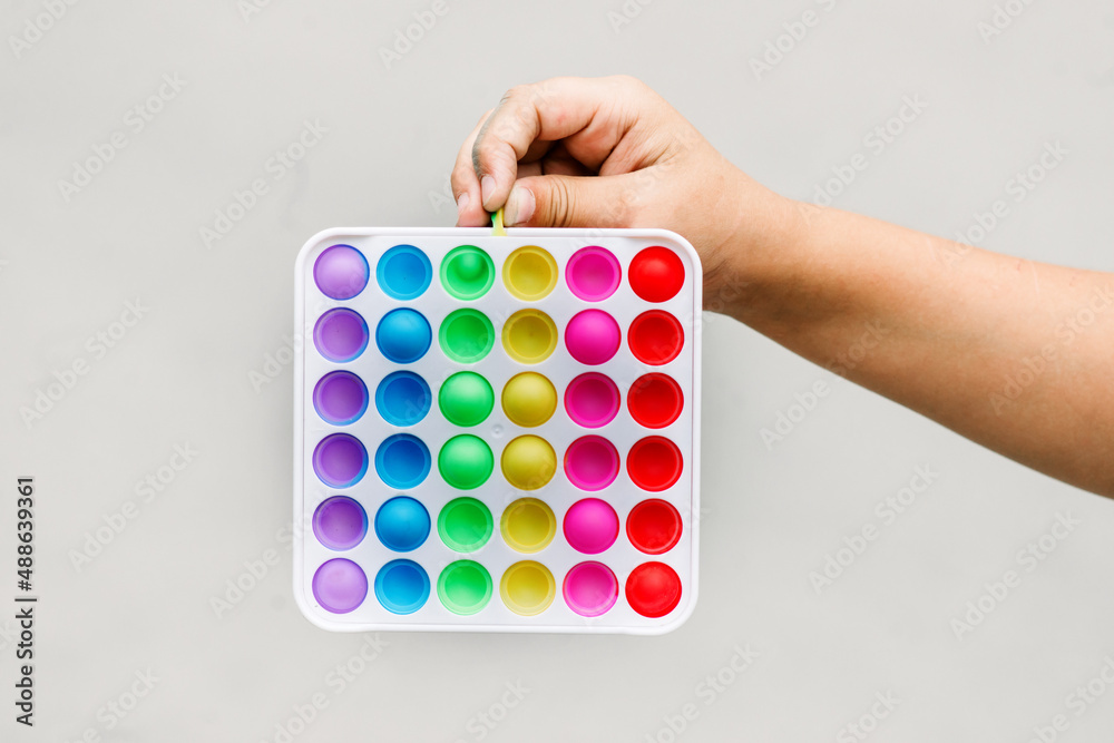 Kid hand holding new trendy pop it fidget toy on grey background. Push pop-it fidgeting game helps relieve stress.